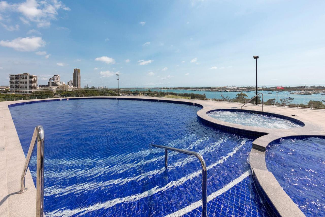 南港美利通公寓式酒店 黄金海岸 外观 照片 The photo shows a serene outdoor pool area with a large, blue swimming pool. The pool has clear water and features a gentle curve along one side, and there's a smaller circular hot tub adjacent to it. In the background, there are buildings and a body